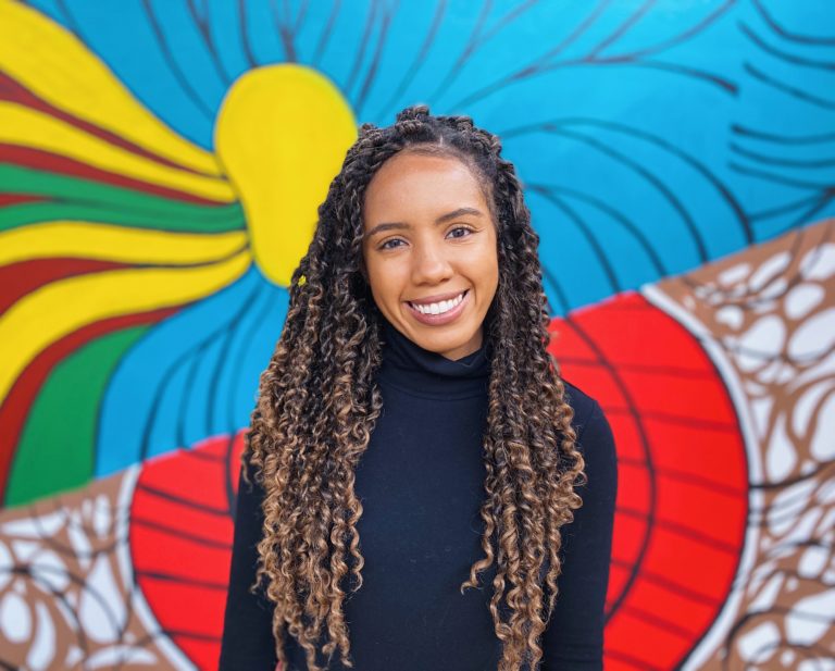 Jacqueline smiles in front of a colorful mural