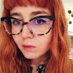 A white cis-woman in her thirties with red hair and large cat-eye glasses.