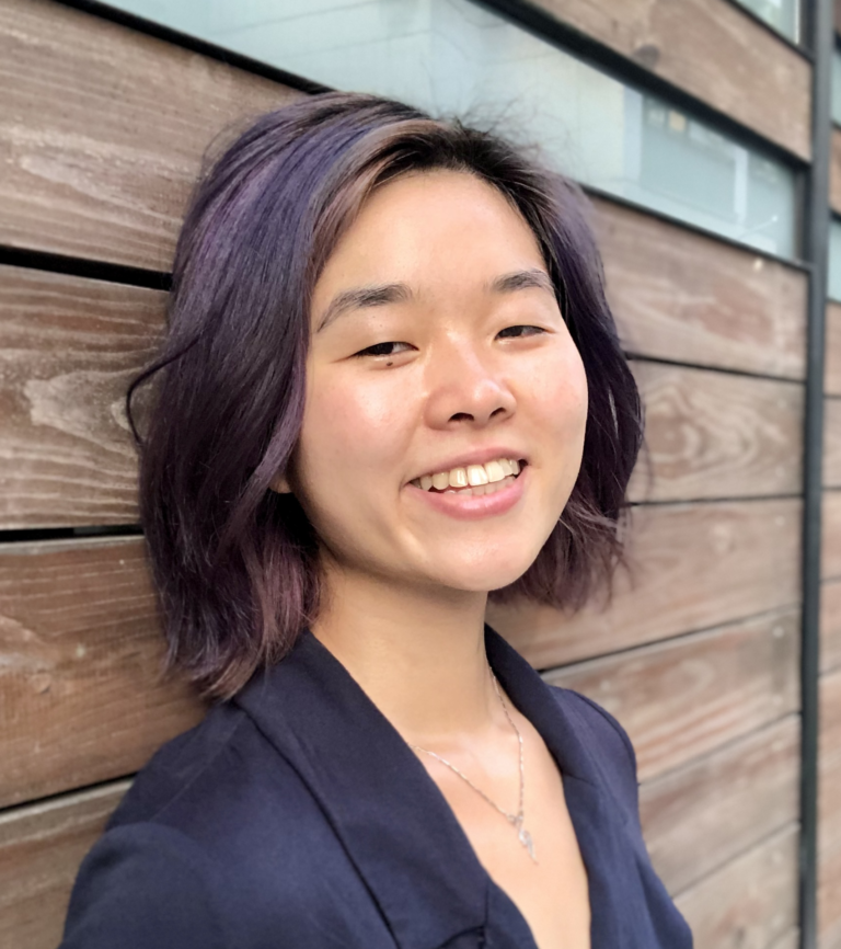 A nonbinary Chinese-American in their twenties, with dark purple hair and wearing a purple jumpsuit.