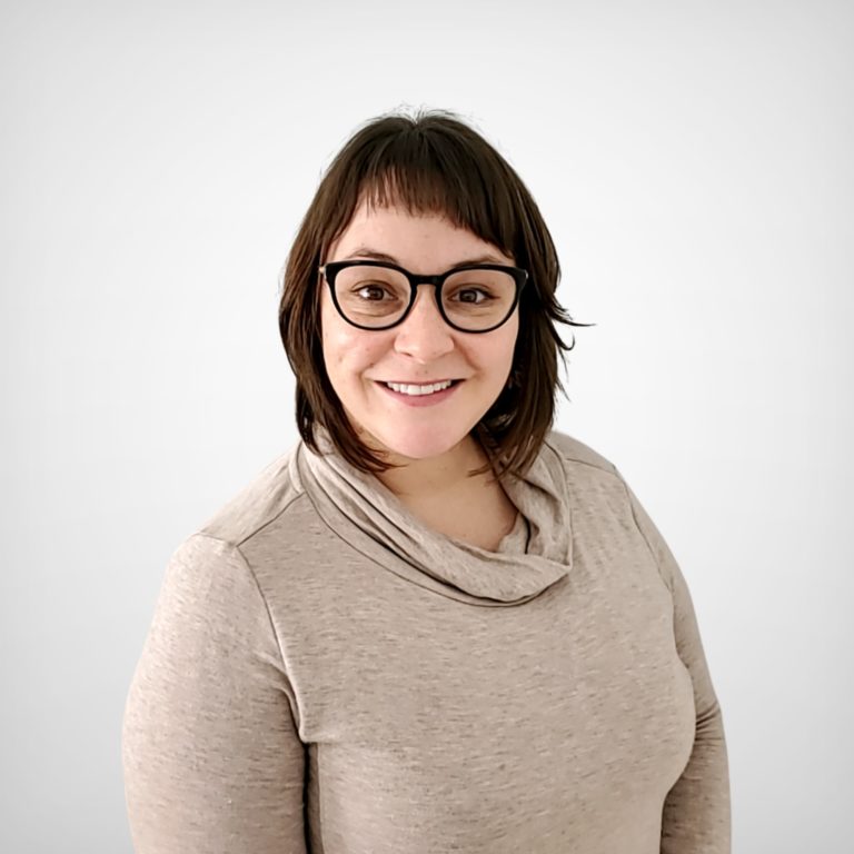 A white woman in her 30s with medium-length brown hair and wearing black glasses