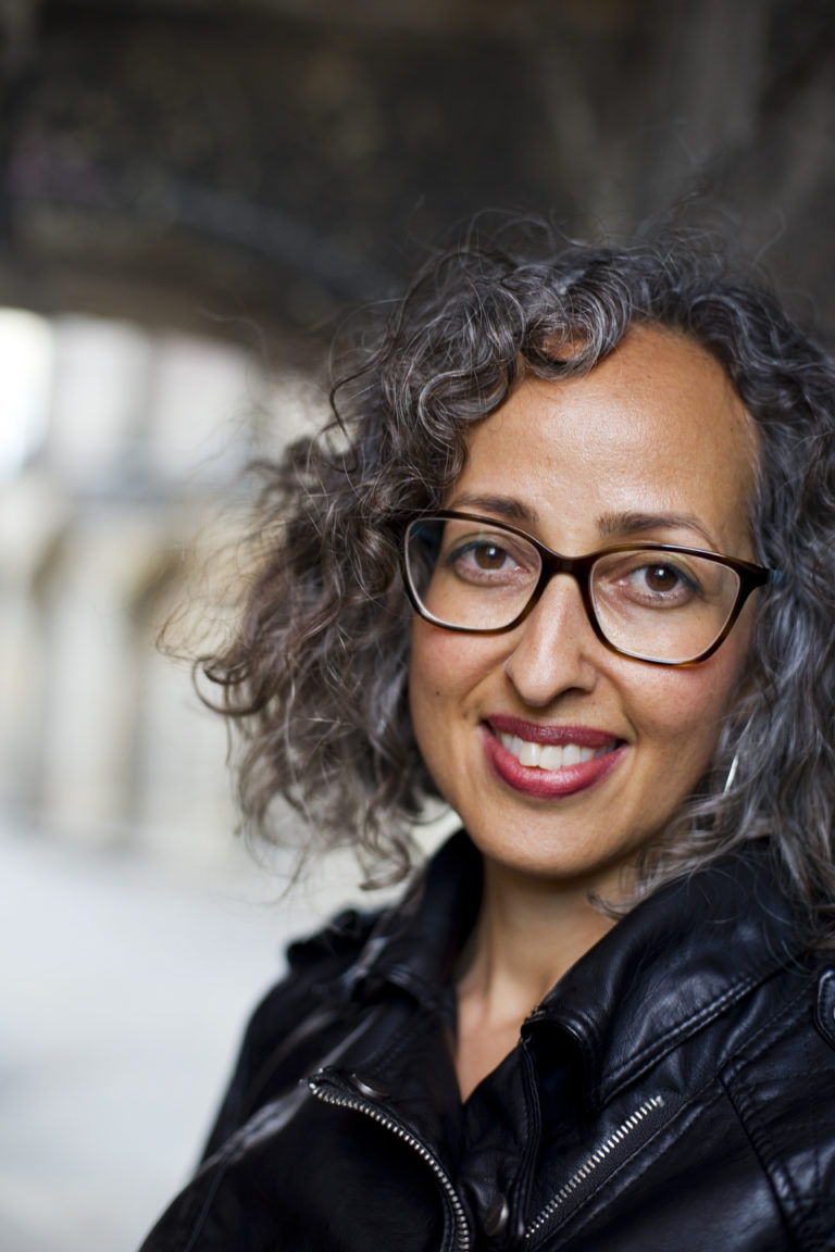 A smiling, middle-aged, mixed Somali American woman with large glasses.