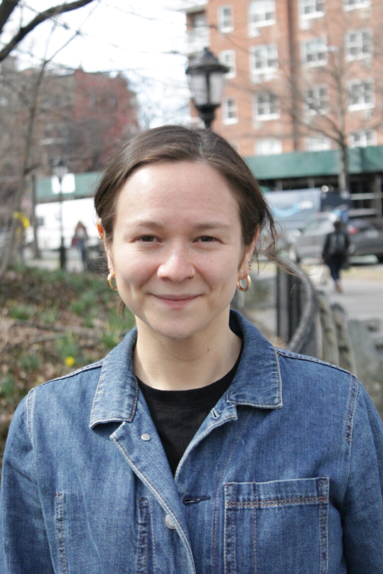 A brunette woman in her 30s wearing a jean jacket standing on a Brooklyn street.